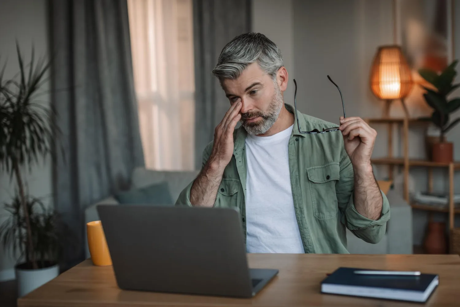 A man at a laptop late in the working day, visibly tired.